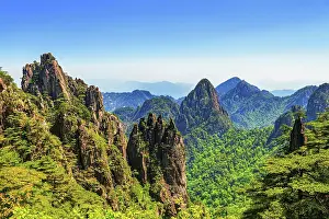Bijia Peak is viewed from a distance, highlighting its distinctive shape amid surrounding green hills and rocky mountains under a clear blue sky bijia peak viewed distance