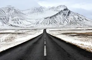 Road Marking Prints: Black tarmac road leading towards snow covered mountains in winter, South Iceland