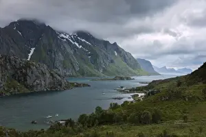 Blue lights and clouds on the calm sea surrounded by rocky peaks at night, Tangstadpollen