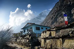 Trek Prints: Blue teahouse and prayer flags under dramatic clouds along the trekking route in Langtang Valley