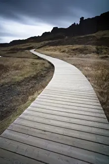 Wooden Walkway Prints: Boardwalk meandering towards rugged cliffs and stormy sky at Thingvellir National Park near Reykjavik