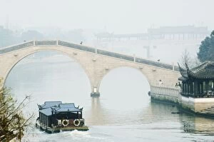 A boat passing through a stone arched bridge on Waicheng River with Wumen bridge behind