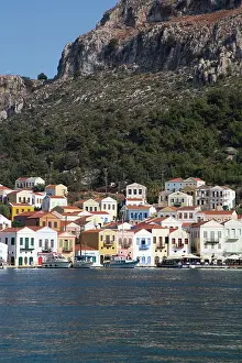 Docked Prints: Boats in Megisti Bay near colorful houses along the coast of Kastellorizo Island in Greece under clear blue skies