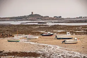 Guernsey Prints: Boats rest on sandy shore at low tide with Fort Saumarez in the distance in Guernsey