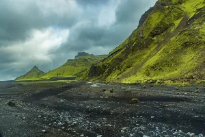 Glacier Prints: Bright green moss covers volcanic cliffs by the glacier in southern Iceland with black sand riverbed below