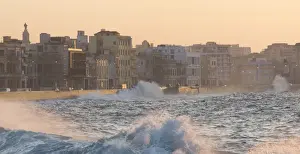 Sea Wall Prints: Buildings along The Malecon bathed in soft evening sunlight with large waves crashing against the sea wall
