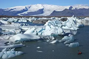 Kayaking Prints: Canoeist paddles between icebergs on glacial lake at Jokulsarlon with snow on the massive icecap of Vatnajokull behind
