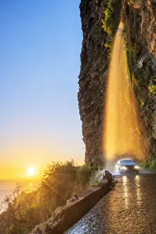 Automobiles Prints: Car passing under Anjos waterfall on slippery coastal road at sunset, Ponta do Sol