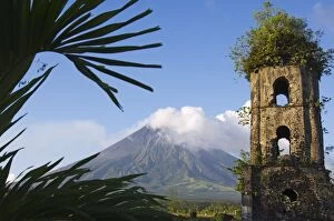 Church belfry ruins and volcanic cone with s moke plume of Mount Mayon