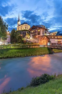 Streetscape Prints: Church and river view in Kaprun at dusk with summer colors in the sky and lights in buildings