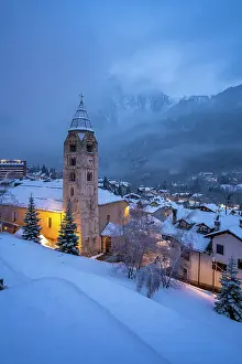 Snowfall Prints: Church of Saint Pantalon, snow covered town centre and mountainous background in winter at dusk