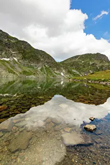 Crystal Prints: Clear mountain lake with rocks visible in Rila Mountains Bulgaria under partly cloudy sky and snow patches on slopes