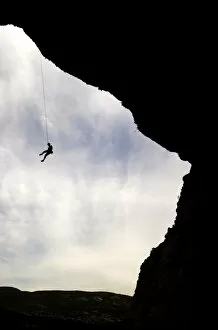 A climber is lowered from a the edge of a huge cave in the Mascun Gorge