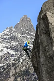Rock Climbing Prints: Climber on steep rock face in the background blue sky and peaks of the Alps, Masino Valley