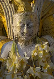 Close up of small Buddha figure with flowers round the neck in the Shwedagon Paya