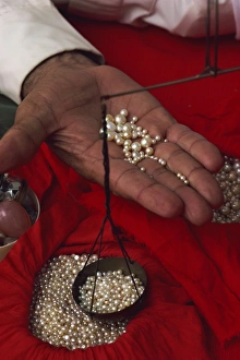 Pearl Prints: Close-up of hand displaying pearls with weighing scales, in the pearl souk