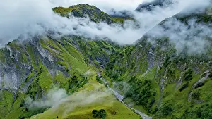 Flowing Prints: Clouds cover green mountains and rocky cliffs in Tschinglengorge during a misty day in Sardona National Park