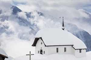 Ski Resort Prints: Clouds above the mountain huts and church covered with snow, Bettmeralp, district of Raron