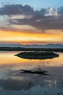Clouds and traditional rowing boat reflecting in the water at sunset, Inle Lake