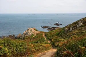 Trail Prints: Coastal path leads down to cliffs and ocean at Pleinmont Point with afternoon light