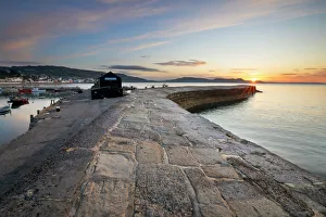 Glowing Prints: The Cobb with the cliffs of Jurassic Coast at sunrise, Lyme Regis, Dorset, England