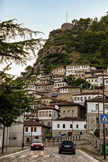 Vehicles Prints: Cobbled streets of Berat show cars driving under Ottoman houses and toward Kala Castle on a sunny day in Albania