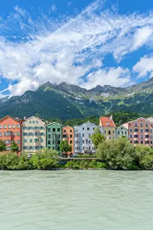 Riverside Prints: Colorful buildings along River Inn on a sunny summer day with mountains in the background in Tyrol Region