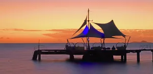 Beachfront Prints: Colorful sunset over the ocean and a pier with a large tent structure near a hotel in Praslin Seychelles