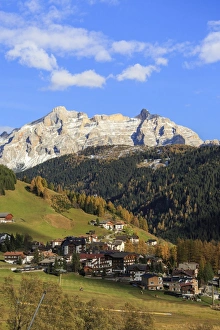 Colourful woods frame the village and the high peaks in autumn, Gardena Valley, South Tyrol