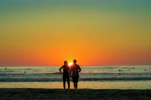 2 People Prints: Couple hold hands on Guiones Beach where people gather to surf and watch at sunset