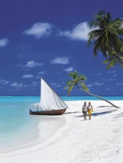 Couple walking on tropical beach and traditional dhoni, Maldives, Indian Ocean, Asia
