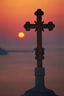 Cross on church dome with setting sun behind