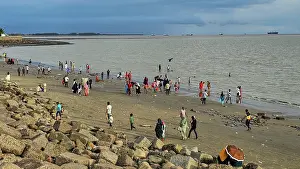 Adults Prints: Crowds enjoy the beach with boats in the background at Chittagong in Bangladesh on a cloudy day
