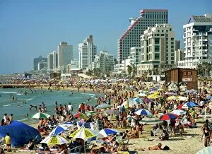 Crowds of tourists on the beach with tall seafront buildings, at Tel Aviv