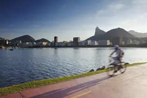 Fitness Prints: Cyclist on pathway around Botafogo Bay with Christ the Redeemer statue (Cristo Redentor) in the background