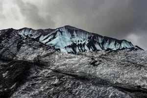 Mountainous Prints: Dark ash and ice layers show volcanic activity on Katla glacier under gray clouds in Iceland