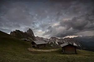 Huts Prints: Dark clouds on green meadows and huts of the Odle mountain range seen from Seceda
