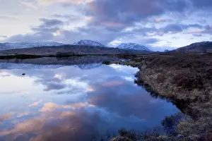 Dawn view of Loch Ba reflecting the sky and distant snow-capped mountains