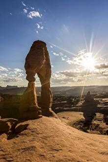 Delicate Arch with sun and clouds at golden hour, Arches National Park, Moab, Grand County