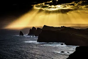 Glow Prints: Dramatic coastline and rocks at sunset in Madeira Portugal with sun rays shining through clouds