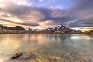 Lombardy Prints: Dramatic sky at sunrise over Tresero peak reflected in lake Manzina, Valfurva, Valtellina