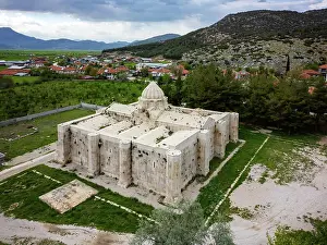 Drone Prints: Drone view shows Suruz Caravanserai in Turkey surrounded by green fields and mountains under a cloudy sky