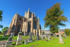 Spires Prints: Dunfermline Abbey stands tall in the sunlight surrounded by gravestones and green grass in Dunfermline