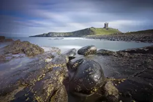 Dunstanburgh Castle bathed in afternoon sunlight with rocky coastline in foreground