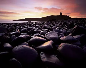 Surface Level Prints: Dunstanburgh Castle at sunrise from Boulderfield at Embleton Bay, Northumberland
