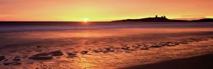 Dunstanburgh castle at sunrise, view across Embleton Bay, Northumberland