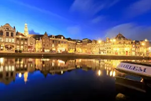 Dusk lights up typical houses reflected in a canal of the River Spaarne, Haarlem