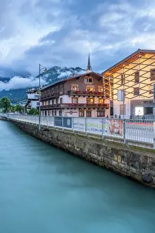 Mountainous Prints: Dusk view of Kaprun town and river in summer with buildings along the water in Salzburg Austria