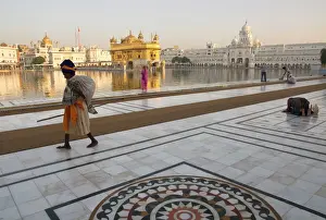 National Famous Place Prints: Elderly Sikh pilgrim with bundle and stick walking around holy pool