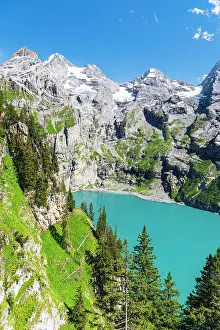 Kandersteg Prints: Elevated view of the crystal blue water of the lake of Oeschinensee among pine trees and alpine peaks covered with snow